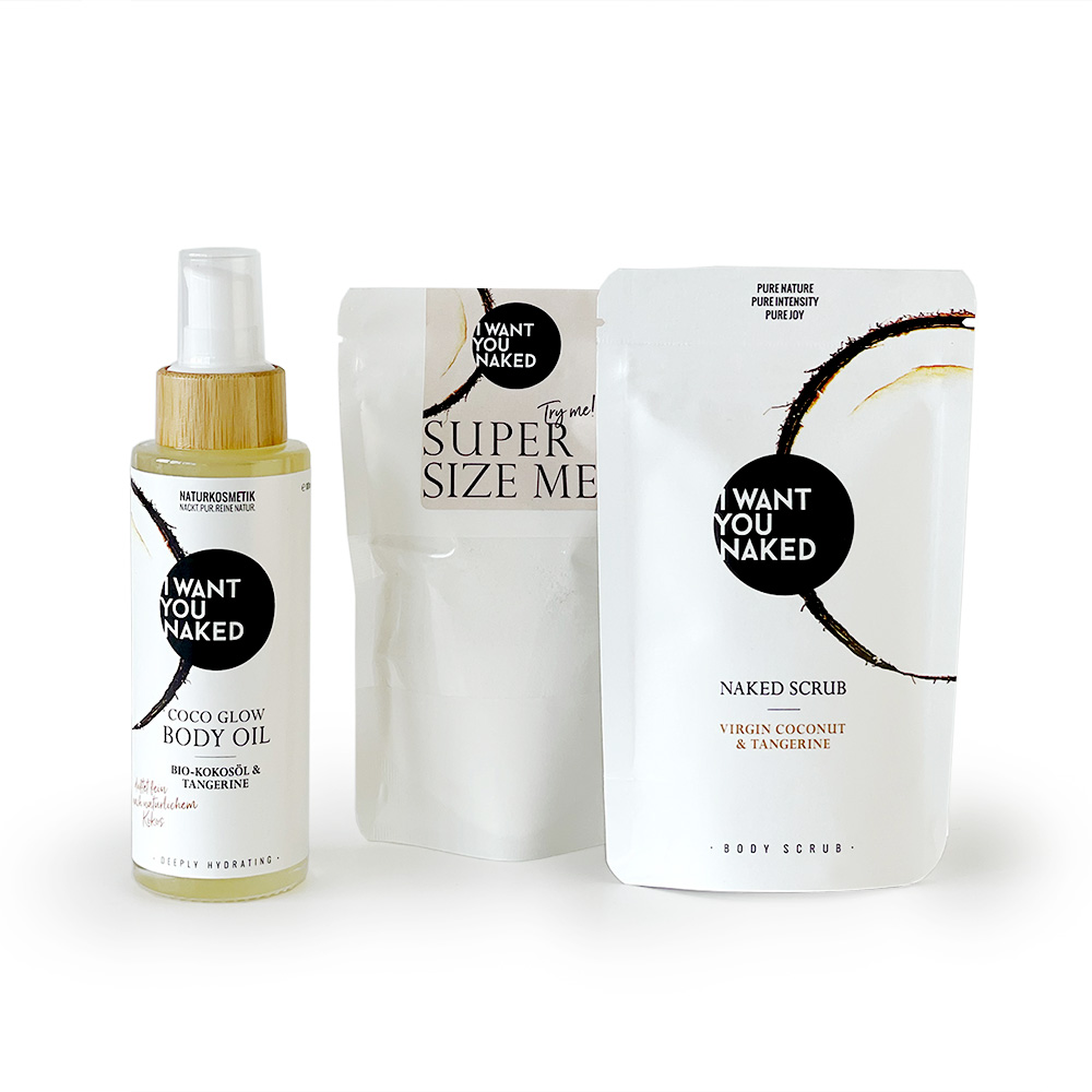 SP-BXC-FL_0010101392065_CocoGlow_02_LOW Drei Produkte von 'I Want You Naked': Körperöl, Peeling und Körperpeeling in weißer Verpackung mit schwarzem Logo.