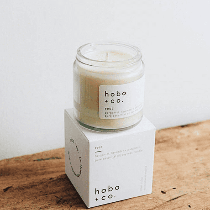 hobo-co-rest-essential-oil-candle-120ml_optimized Hobo+Co Rest Duftkerze mit ätherischen Ölen, 120ml, auf Holztisch vor weißer Wand.