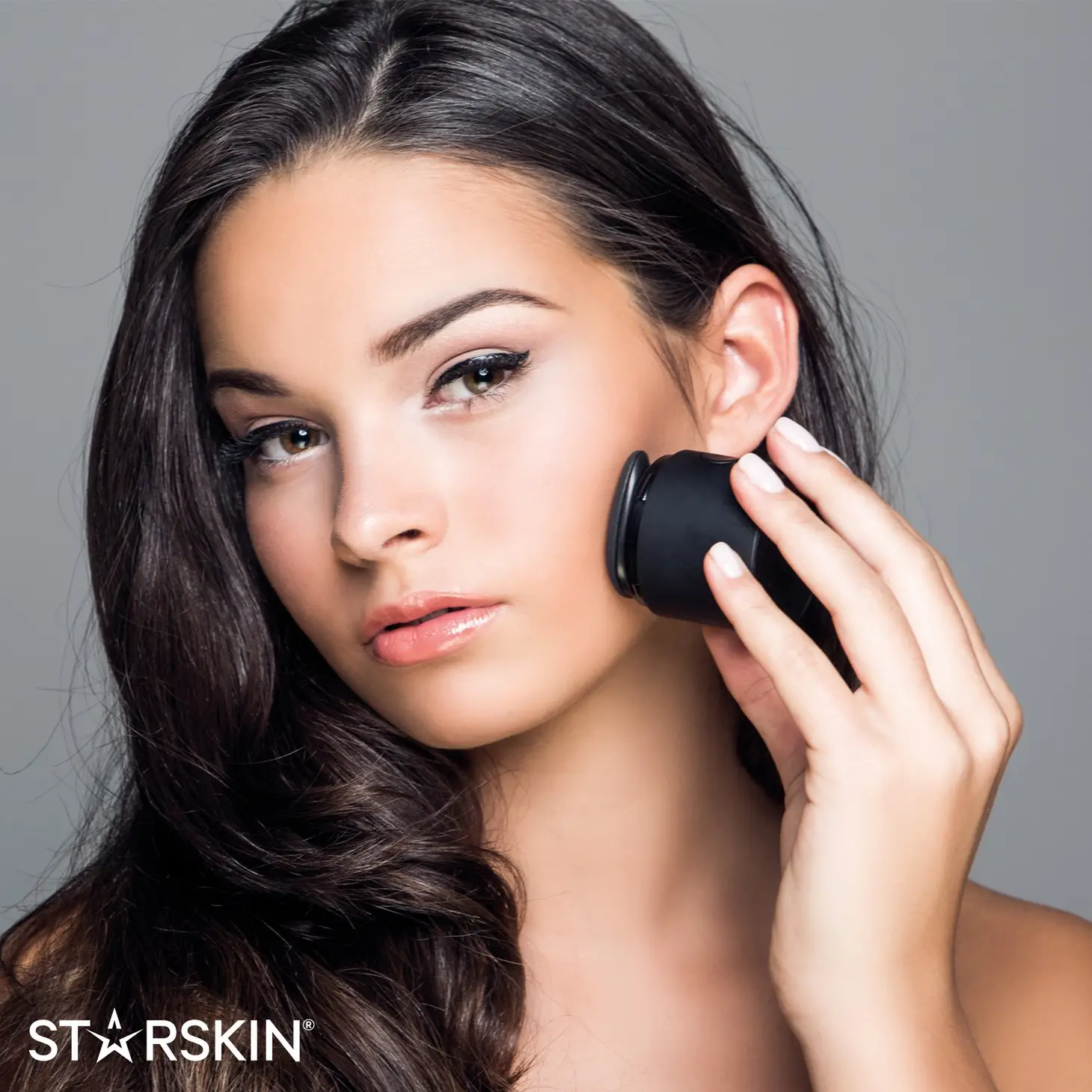 C1BE1EDE-D119-498C-A052-5A9E0DFDE571 Frau verwendet ein schwarzes Schönheitsgerät auf ihrem Gesicht. Text: STARSKIN.