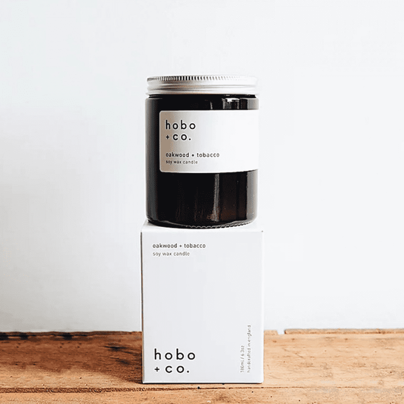 Hobo + Co. Oakwood & Tobacco Duftkerze auf Holzoberfläche, 180ml Glas und Verpackung.