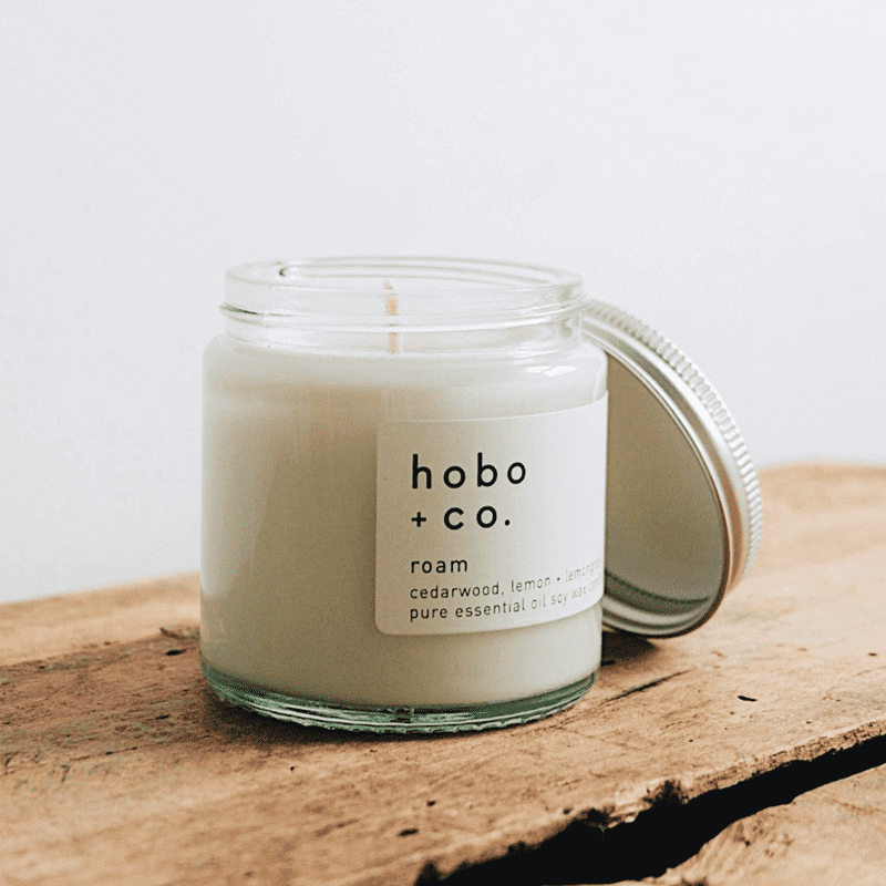 hobo-co-roam-essential-oil-candle-120ml_optimized Eine geöffnete Duftkerze von hobo + co. auf einem rustikalen Holztisch.