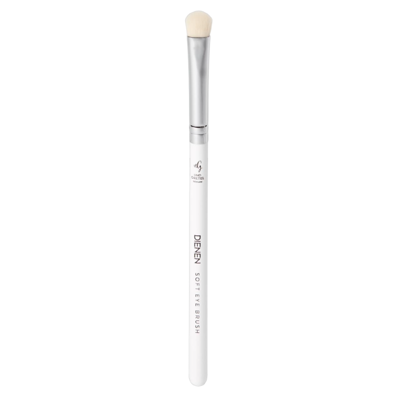 UND-GRETEL-DIENEN-EYE-SOFT-BRUSH-2_3 Ein weißer Schminkpinsel mit silbernem Griff und weichen Borsten, beschriftet mit 'UND GRETEL DIENEN SOFT EYE BRUSH'.