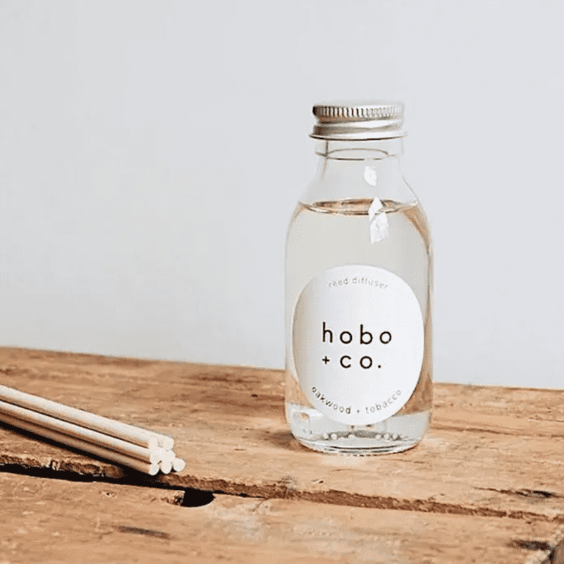 Hobo + Co. Oakwood Tobacco Reed Diffuser auf einem Holztisch mit Duftstäbchen.
